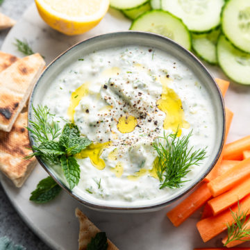 tzatziki dip in bowl with cucumber and pita bread around it
