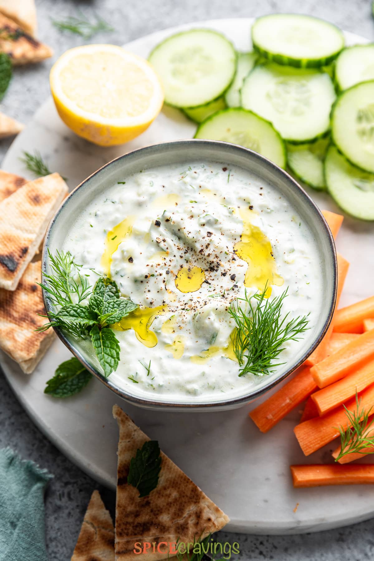 tzatziki dip in bowl with cucumber and pita bread around it