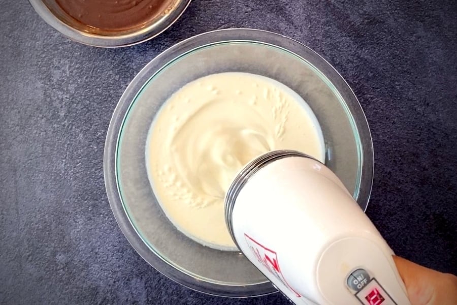 electric mixer whipping cream in glass bowl