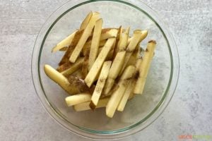 sliced potatoes with seasoning in glass bowl