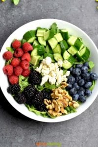 arugula, cucumbers, raspberries, blueberries, blackberries, walnuts, feta in white bowl
