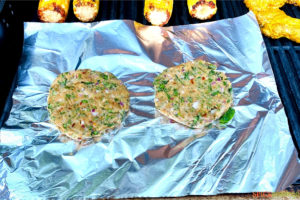 two chicken patties on aluminum foil on an outdoor grill