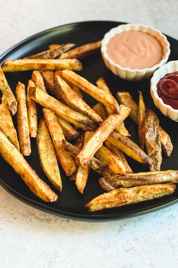homemade french fries on black plate with fry sauce and ketchup in white bowls