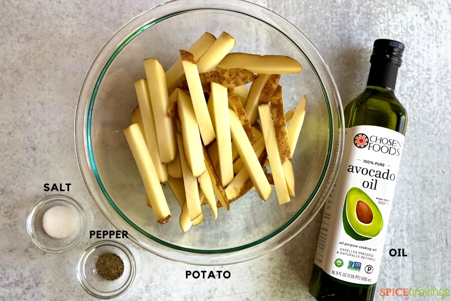 sliced potatoes in glass bowl, avocado oil jar, salt and pepper in two small bowls