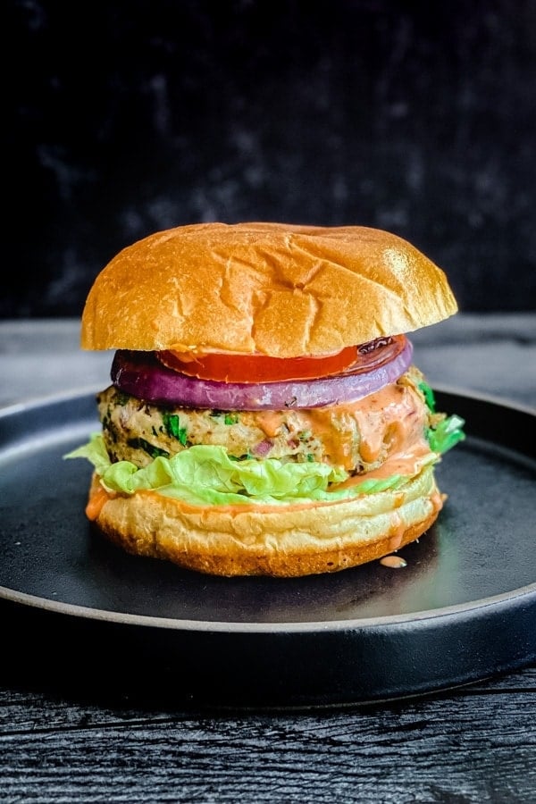 indian spiced chicken burger with lettuce, tomato, onion, sriracha mayo on bun on black plate
