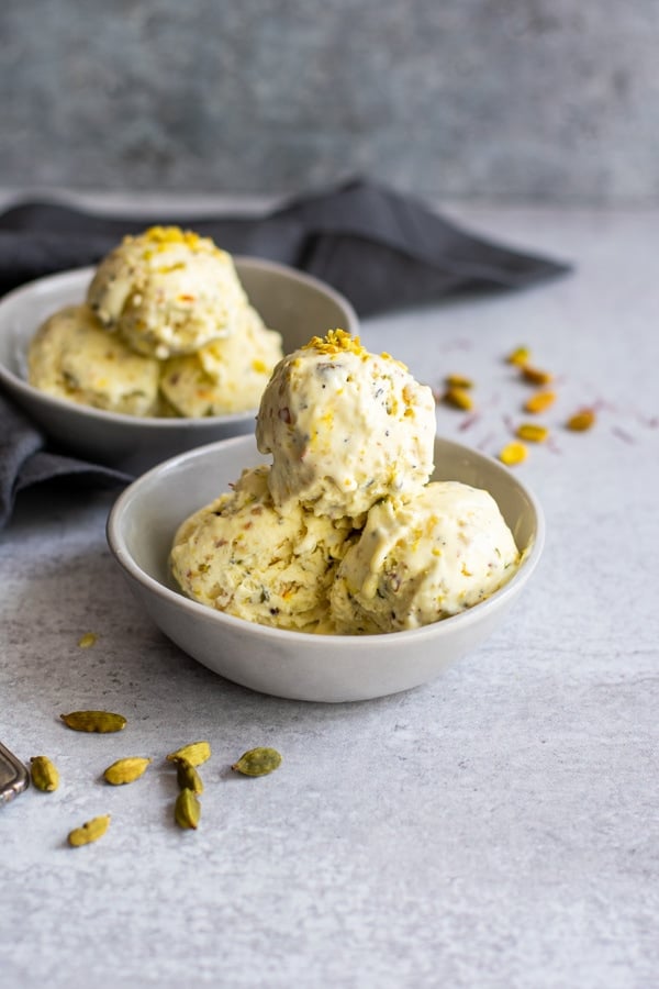 scoops of kulfi ice cream in two white bowls topped with chopped nuts