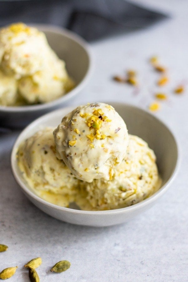 three scoops Indian ice cream in white bowl with chopped pistachios