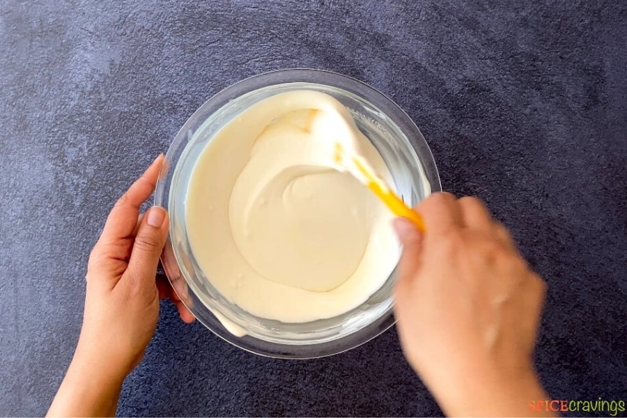 two hands stirring ice cream mix in glass bowl