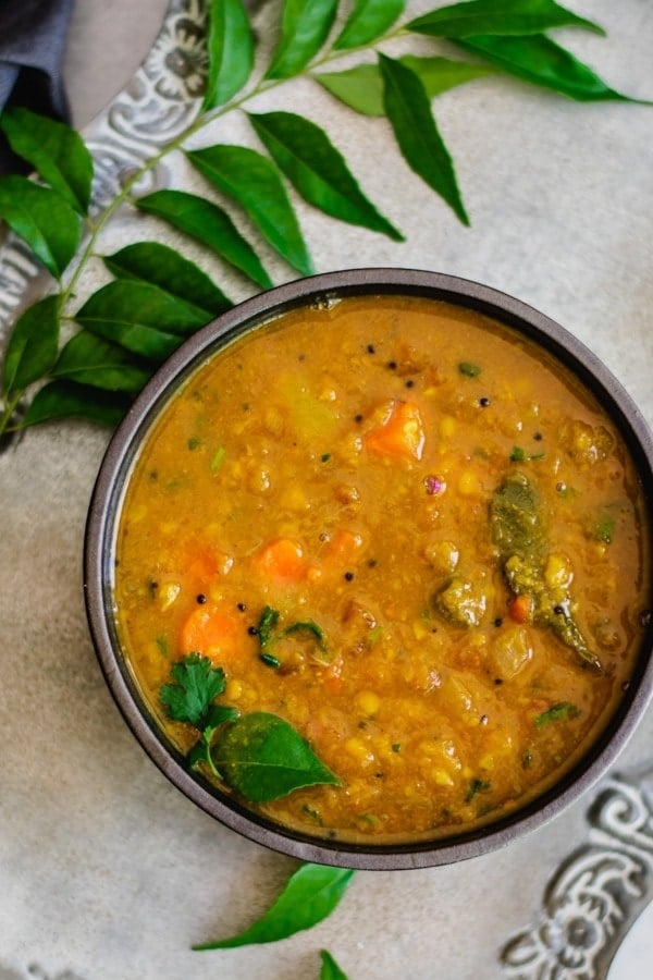 instant pot sambar recipe in gray bowl with curry leaves on the side