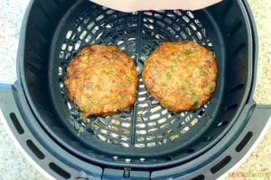 two chicken burger patties cooking in air fryer basket
