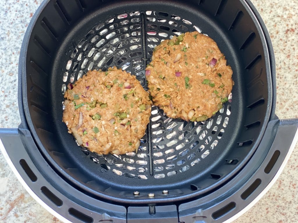 two chicken burger patties cooking in air fryer basket