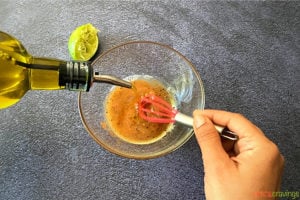 pouring olive oil into small glass bowl while whisking