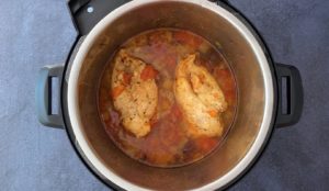 two chicken breasts simmering in spicy tomato onion sauce in Instant Pot