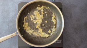 minced garlic and ginger in stainless steel skillet on hot plate