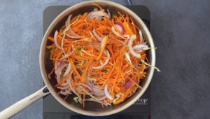 sliced carrots and onions in stainless steel chef pan on hot plate