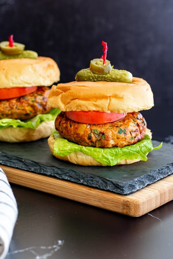 two mexican chicken burgers on buns with lettuce, tomato and skewered with pickle