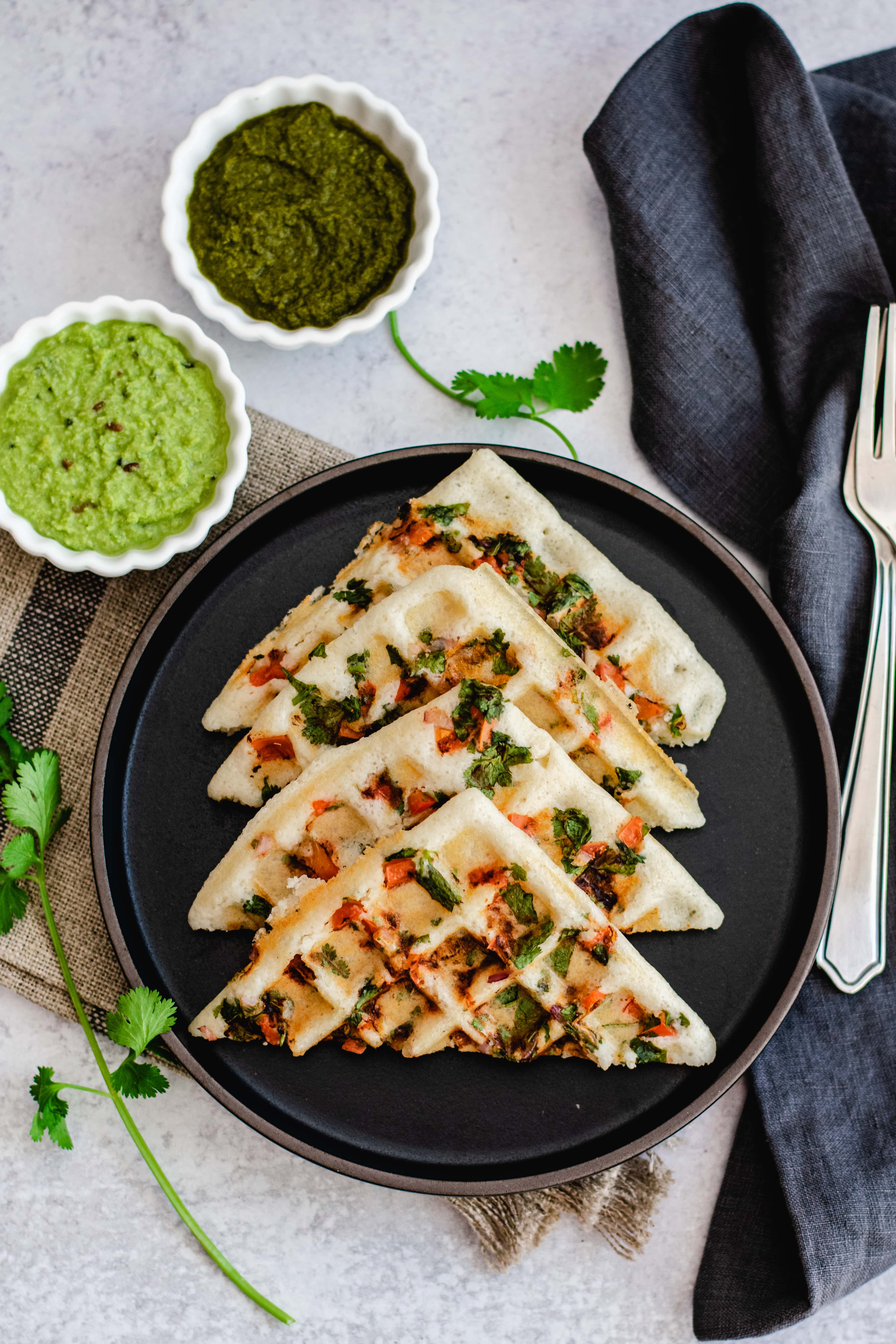 uttapam waffle recipe on black plate with two bowls of chutney on side