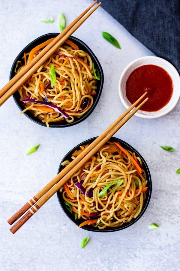 vegetable chow mein recipe in two small black bowls with chopsticks and sauce on side