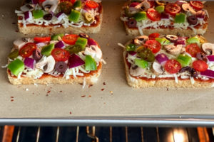 slices of bread, cheese and vegetable toppings on parchment-lined baking sheet in oven