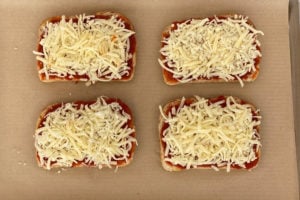 shredded cheese and tomato sauce on four slices of bread on parchment-lined baking sheet