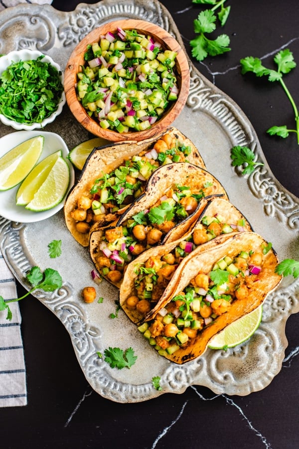 chana masala tacos with cucumber salsa on silver serving platter with lime wedges and cucumber salsa on side