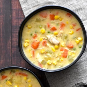 A black bowl with chicken and corn chowder with carrots and celery