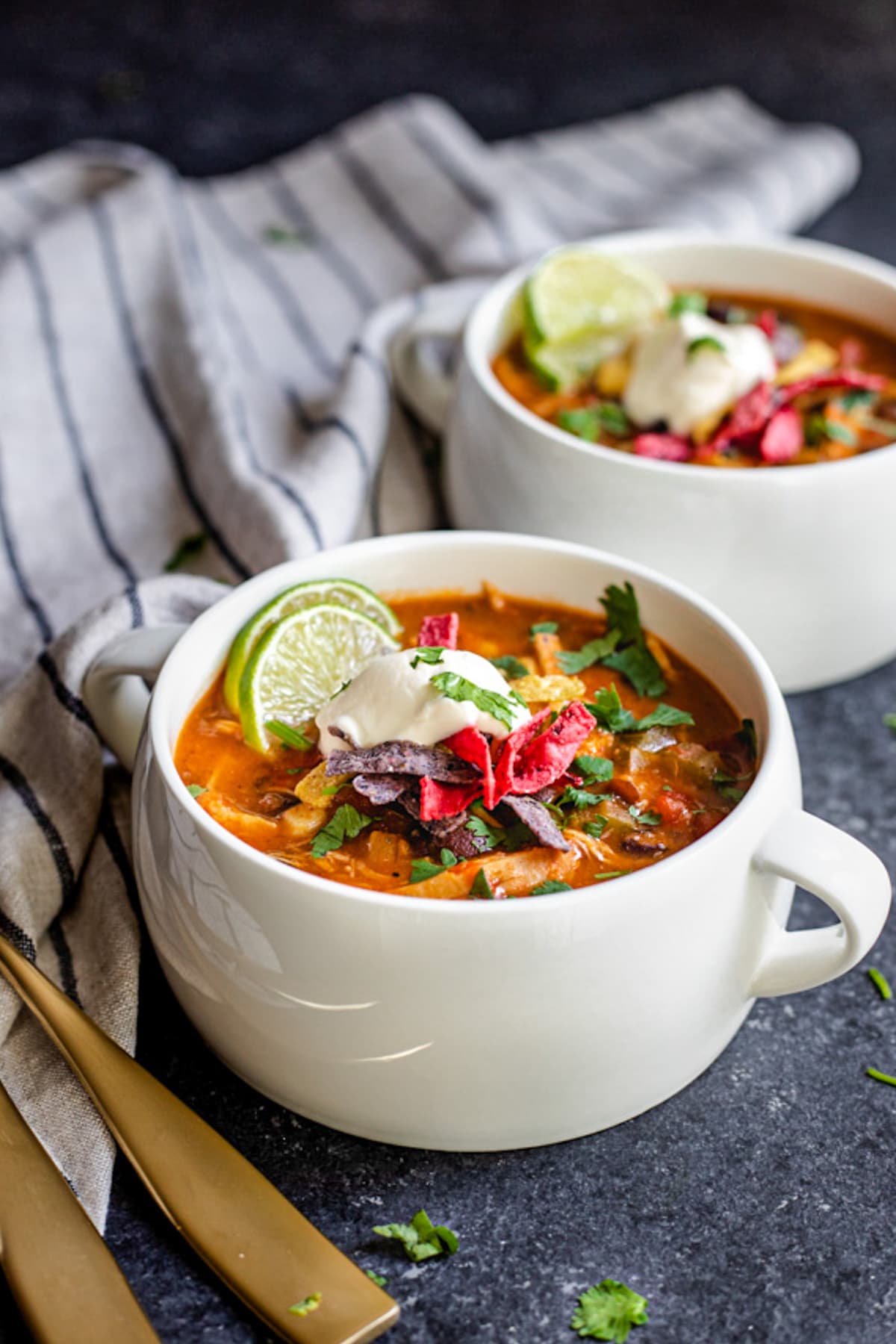 enchilada soup in two white soup crocks topped with sour cream and tortilla strips