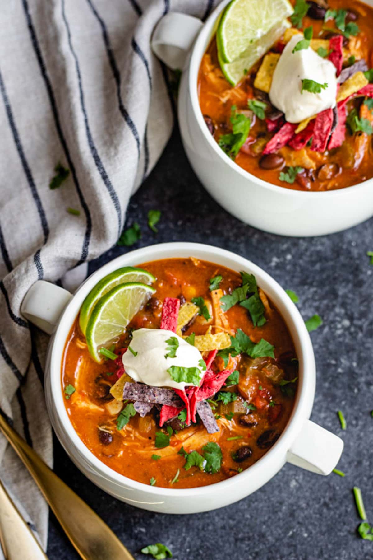 enchilada soup in white soup crock topped with sour cream, cilantro and tortilla strips