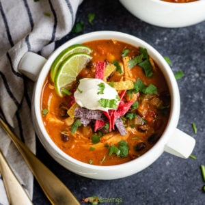 creamy enchilada soup in two white soup crocks topped with sour cream and tortilla strips