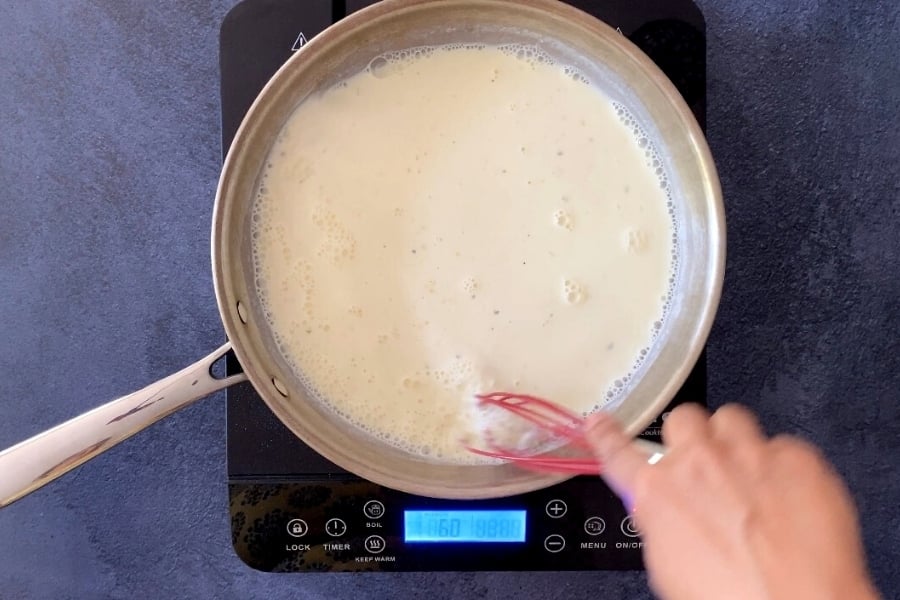 pink spatula stirring thickened milk in stainless steel saucepan