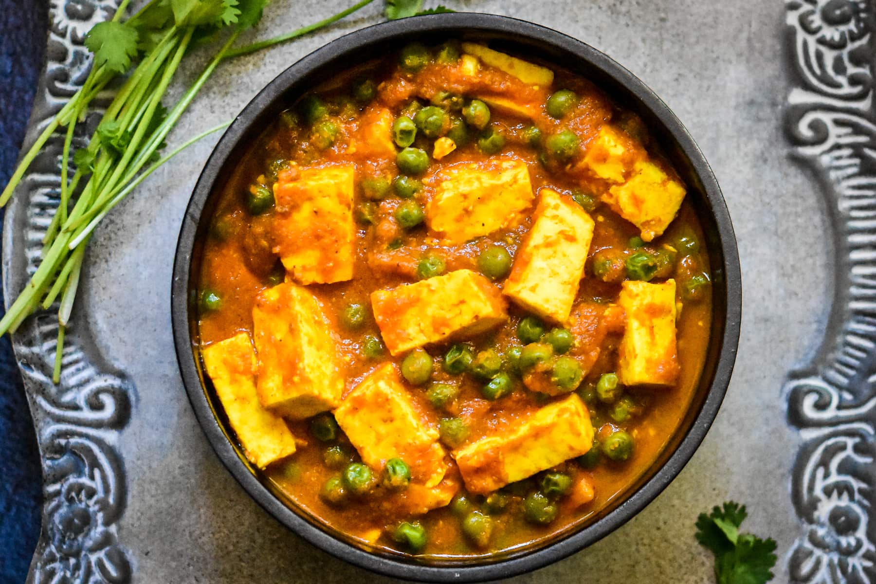 easy mutter paneer recipe in black bowl on silver platter with blue napkin