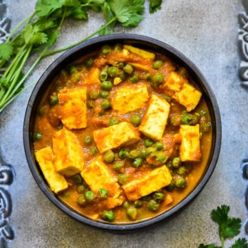 paneer and pea curry in black bowl with cilantro sprigs on silver platter