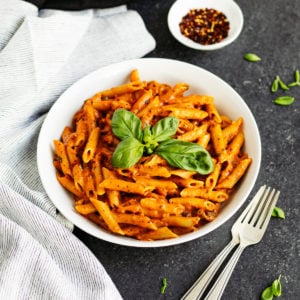 penne vodka recipe in white bowl garnished with fresh basil with two forks on the side