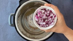 hand holding chopped red onions in small white bowl over instant pot