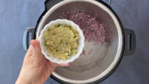 hand holding minced garlic, ginger, chile in small white bowl over instant pot