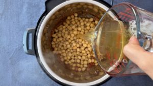 pouring water from measuring cup over chickpeas in instant pot