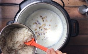 pouring soaked rice into instant pot with simmering milk