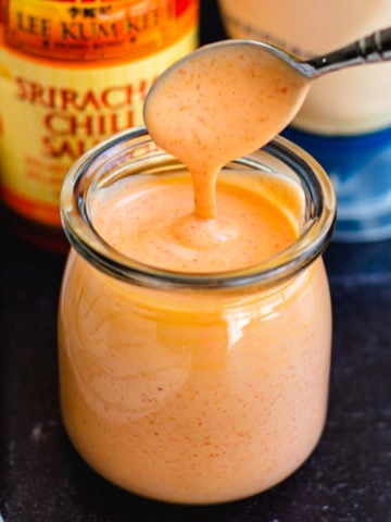 homemade spicy mayo in glass container with spoon and sriracha and mayo bottle in background