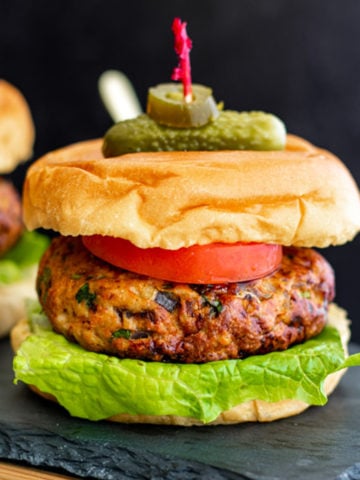 mexican style chicken burger on buns with lettuce, tomato and skewered with pickle