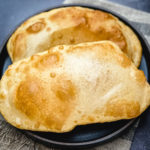 two pieces golden brown fried bhatura on black plate