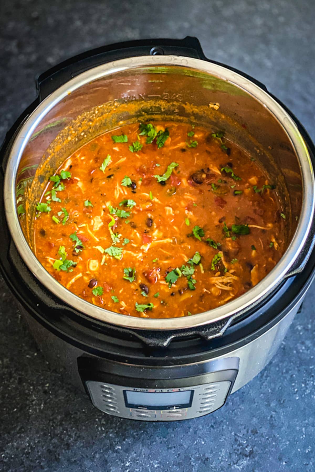 Instant pot filled with enchilada soup with chicken, beans and cilantro
