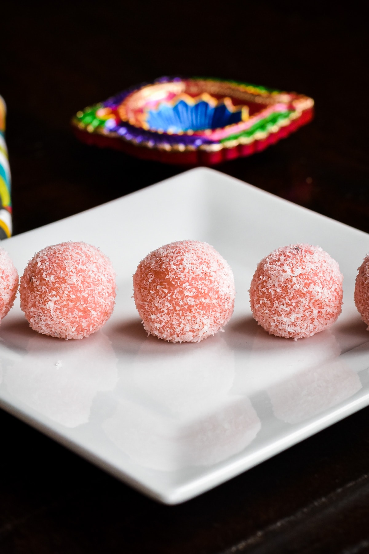 five blush pink coconut fudge balls on white plate with black background