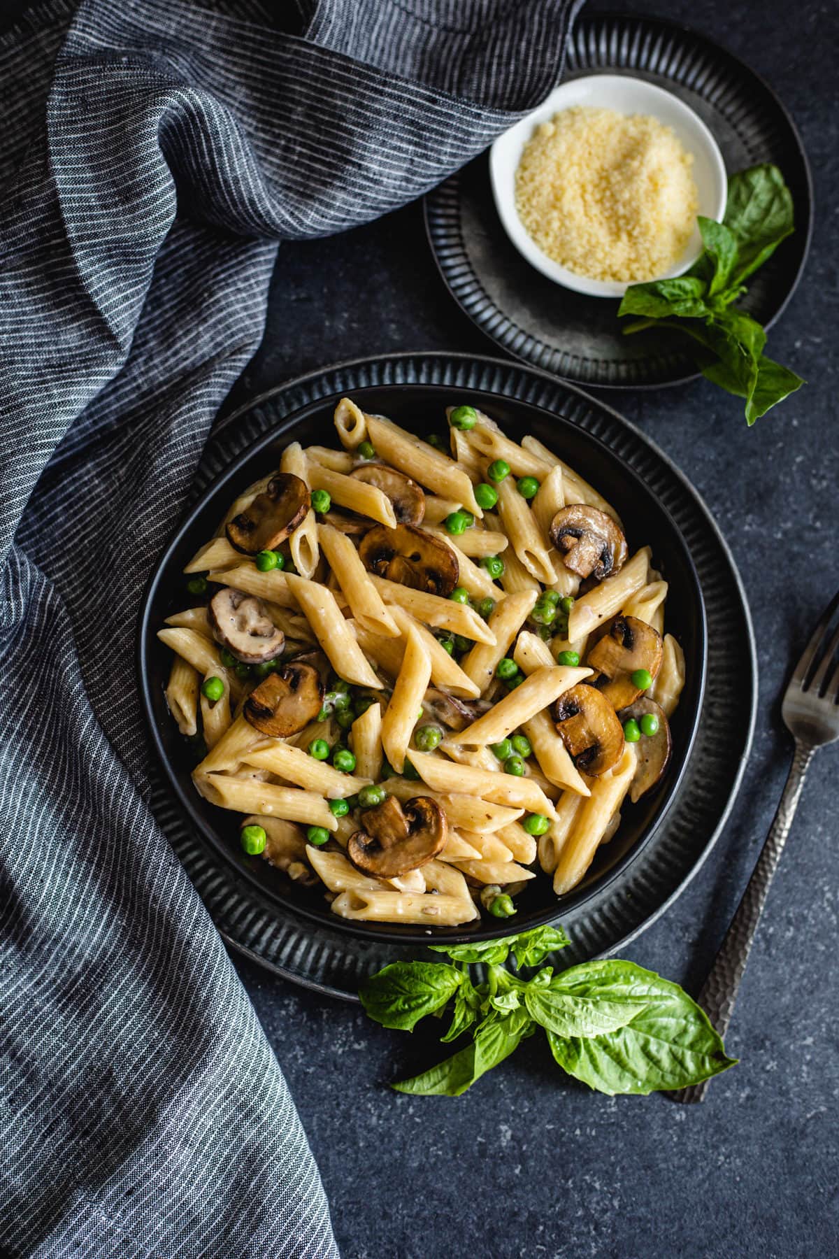 creamy mushroom pasta recipe in black bowl with grated cheese and fresh basil