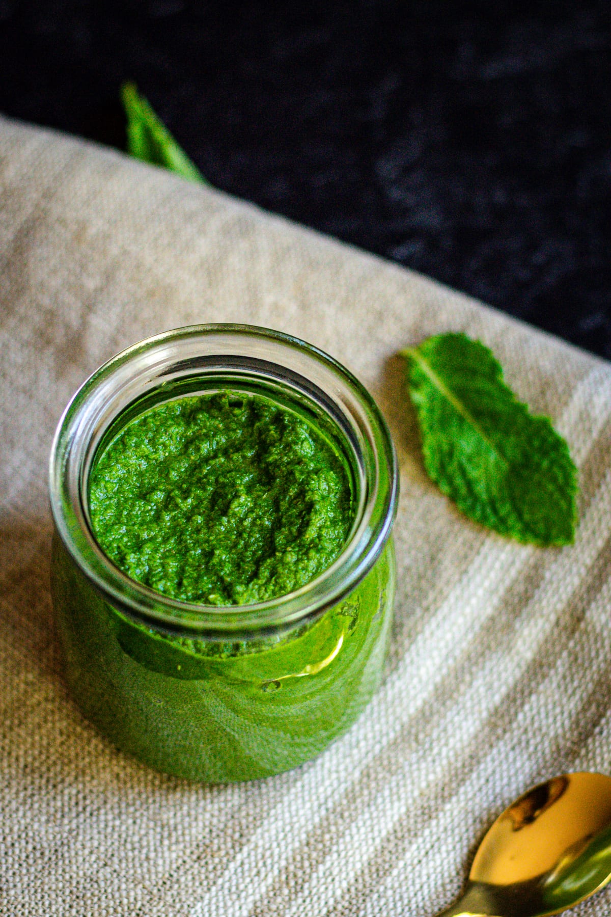 pudina chutney in glass jar with mint leave and gold spoon on the side