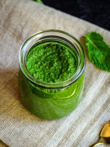pudina chutney in glass jar with mint leave and gold spoon on the side