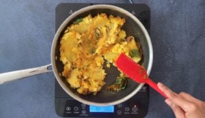 red spatula turning aloo masala filling in nonstick skillet on hot plate