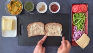 two hands buttering whole grain bread slices with small bowls of condiments on the side
