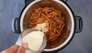 pouring cream from measuring cup into penne and tomato sauce in instant pot