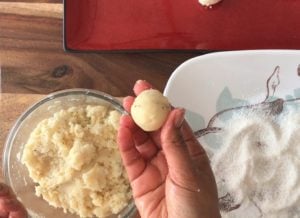hand holding ball of coconut ladoo with dough in glass bowl underneath