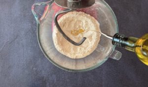 oil pouring into flour in bowl of stand mixer with dough hook